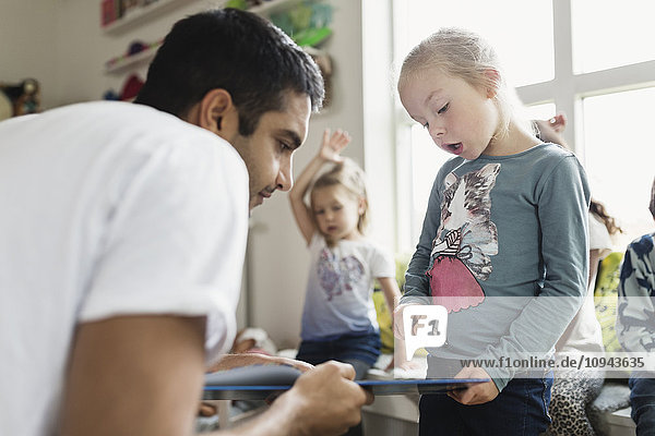 Male teacher and girl looking at book in day care center