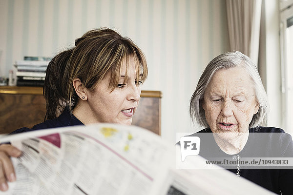 Caretaker with senior woman reading newspaper at nursing home