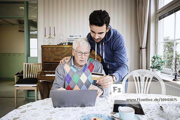 Caretaker and senior man using credit card to shop online