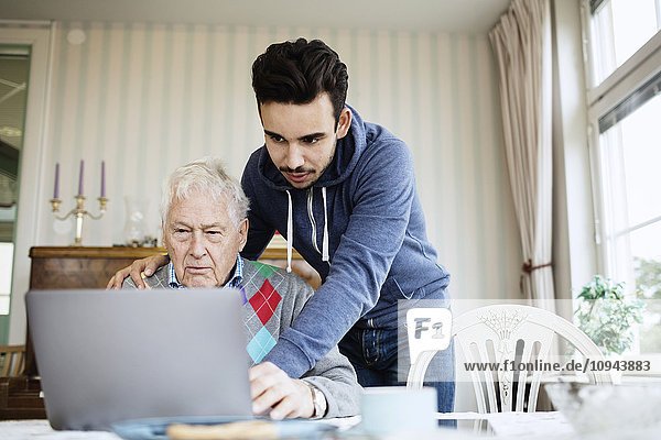 Caretaker unterstützt ältere Männer bei der Nutzung des Laptops im Pflegeheim