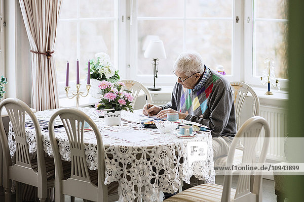 Senior Mann beim Schreiben im Buch am Esstisch im Pflegeheim