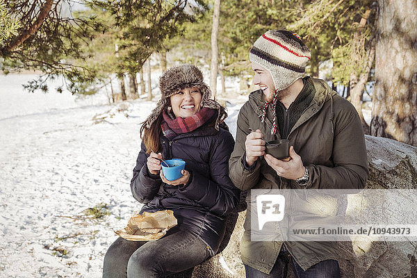 Couple enjoying food while sitting on rock during winter