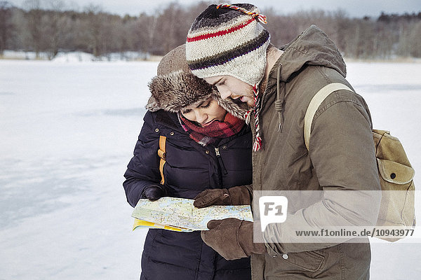 Couple looking at map while standing on field during winter