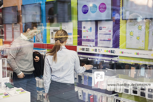 Saleswoman helping customer in buying phone cover seen through glass