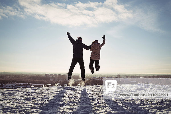 Paar hält Hände beim Springen auf schneebedecktem Berg gegen den Himmel