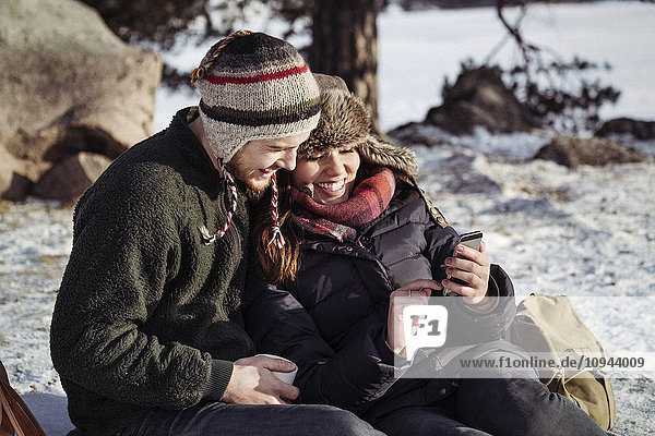 Couple using smart phone while relaxing on snow covered field