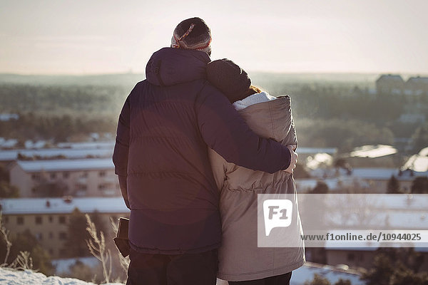 Rear view of couple embracing while standing on mountain during winter