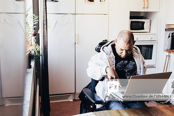 Behinderter Mann mit Laptop im Rollstuhl im Aufnahmestudio