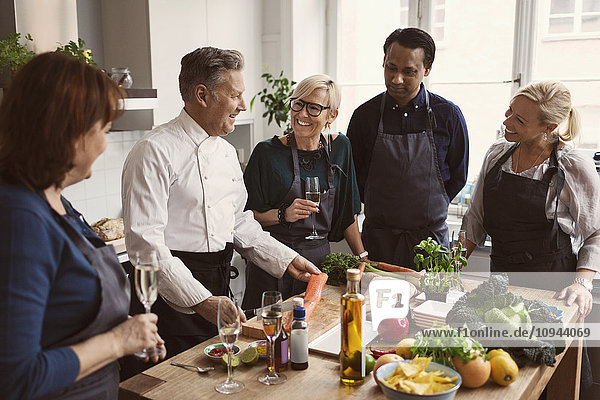 Happy chef preparing food while teaching to students standing at table