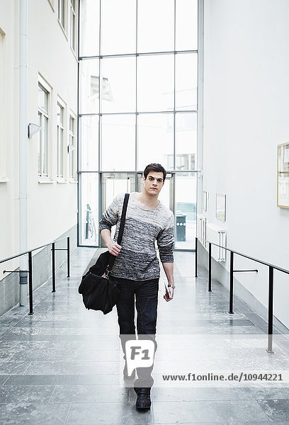 Full length of handsome young man walking carrying bag