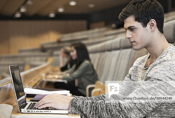 Seitenansicht des hübschen jungen Mannes mit Laptop im Kongresszentrum