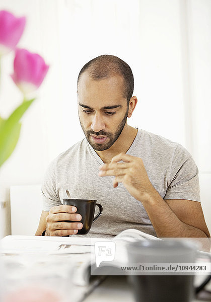 Front view of mid adult man reading newspaper while holding cup of coffee