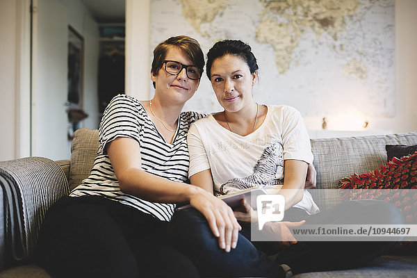 Portrait of smiling lesbian couple sitting in living room at home