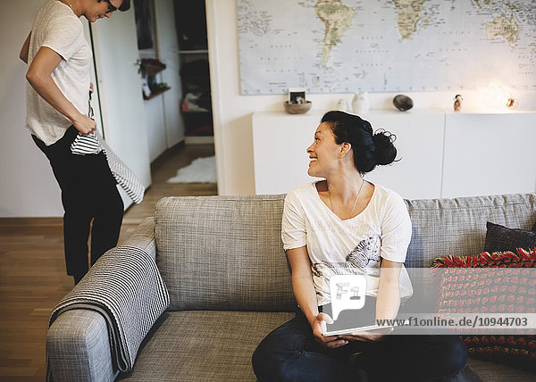 Smiling woman looking at girlfriend holding t-shirt in living room at home