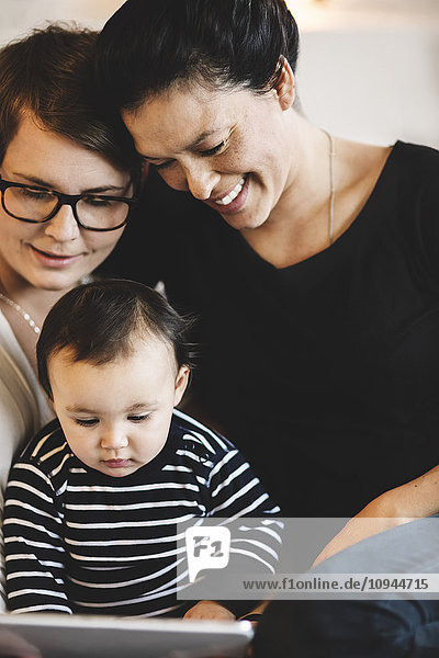 Lächelnde Frauen mit Kleinkind im digitalen Tablett  während sie zu Hause sitzen.