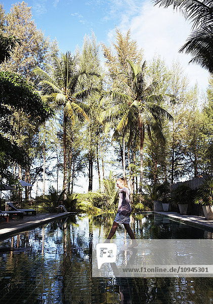 Thailand  woman crossing pool of water with palm trees reflecting
