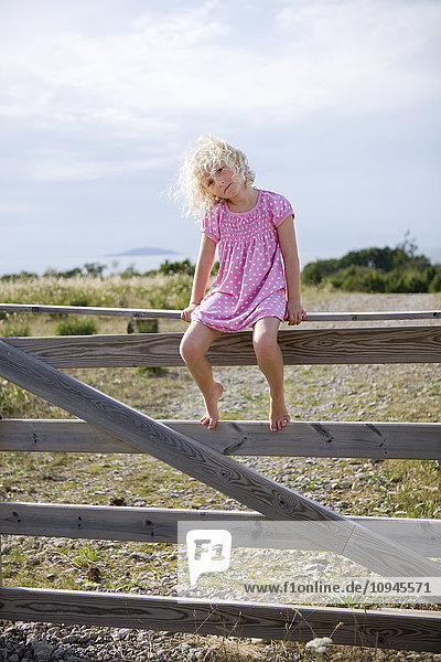 Blonde girl sitting on wooden gate