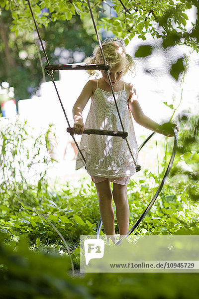Mädchen spielt im Garten mit Schaukel und Schlauch