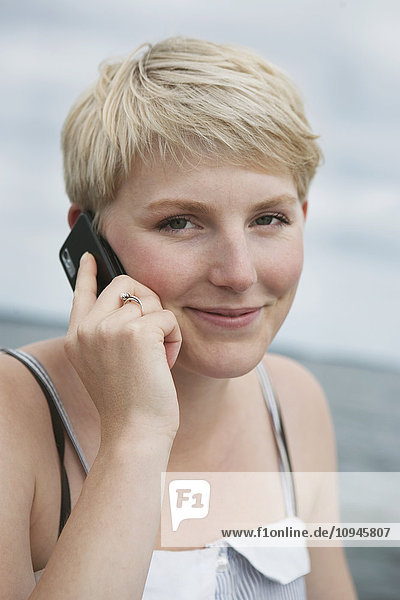 Porträt einer jungen blonden Frau  die mit einem Mobiltelefon spricht