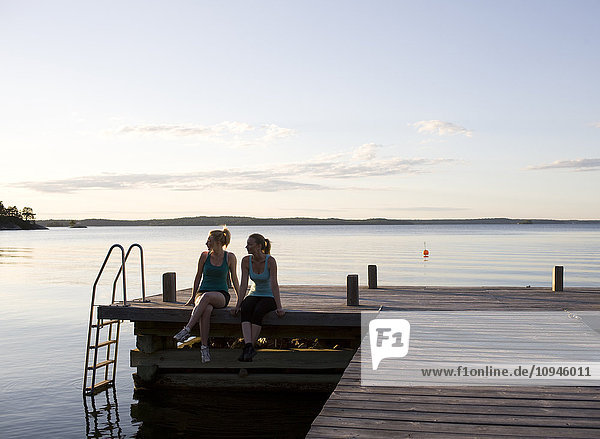 Two women sitting on pier at dusk