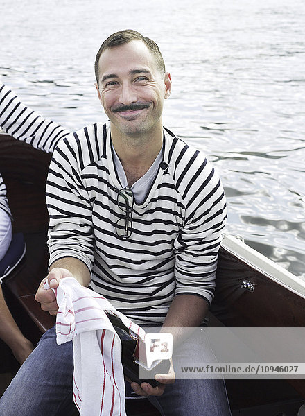 Mann sitzt in einem Boot und hält eine Weinflasche  lächelnd