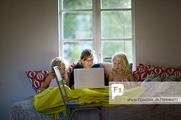 Drei Mädchen sitzen auf dem Sofa und beobachten den Laptop