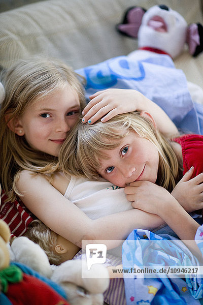 Zwei Mädchen liegen auf dem Sofa zwischen Spielzeug