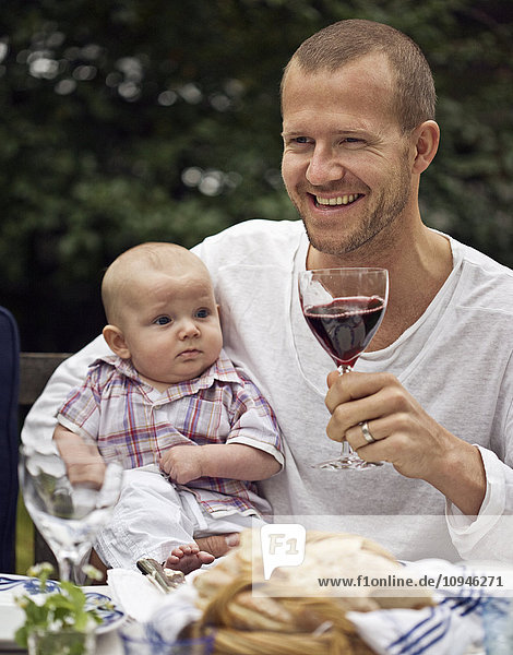 Mittlerer erwachsener Mann stößt mit Wein an und hält einen kleinen Jungen
