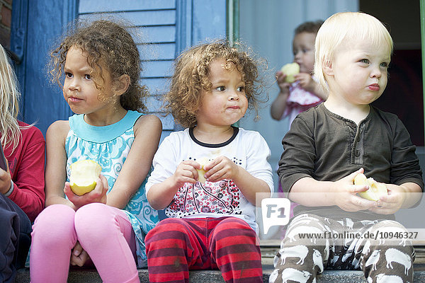 Kinder sitzen auf Stufen und essen Äpfel