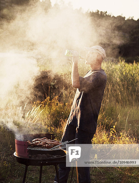 Man drinking beer next to barbecue grill