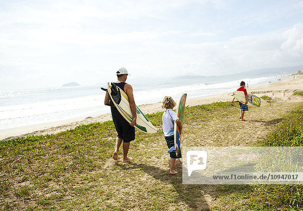Zwei Jungen und ein Mann gehen am Strand mit Surfbrettern spazieren