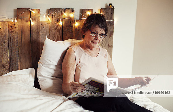 Ältere Frau liest Zeitung im Bett