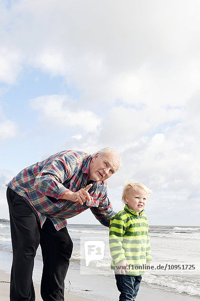 Großvater mit Enkel am Strand stehend