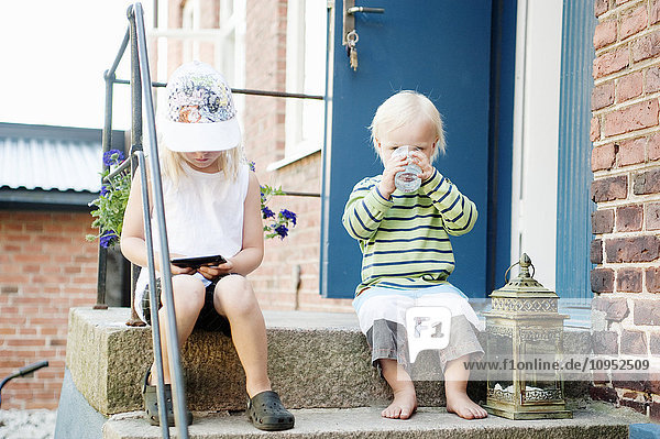 Mädchen und kleiner Junge sitzen auf einer Stufe vor einem Haus