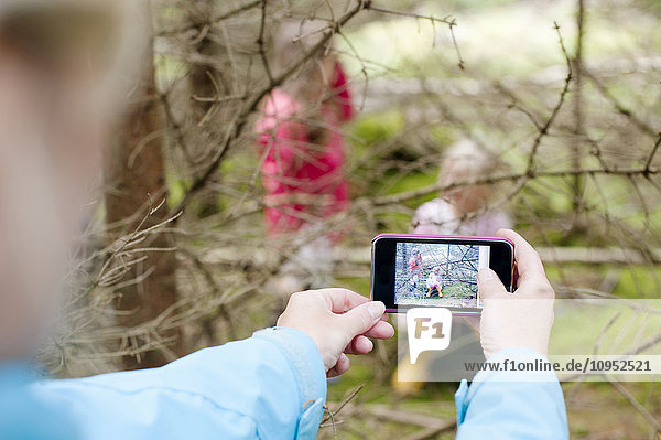 Frau fotografiert Mädchen hinter Baumzweigen