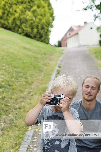 Junge fotografiert im Park mit Vater im Hintergrund