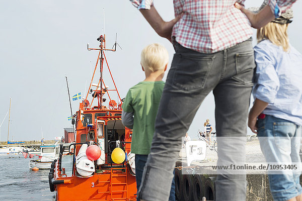 Vater mit Kindern steht im Yachthafen und sieht sich Ausflugsboote an