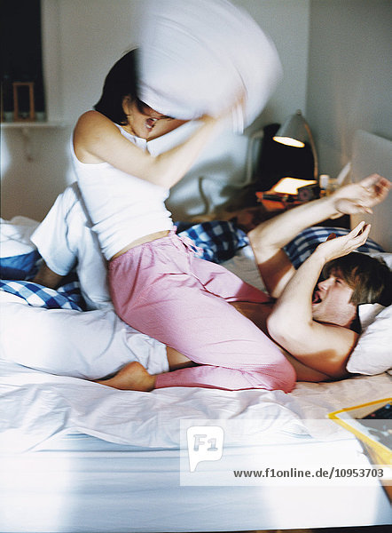 Man and woman having pillow fight in bed.