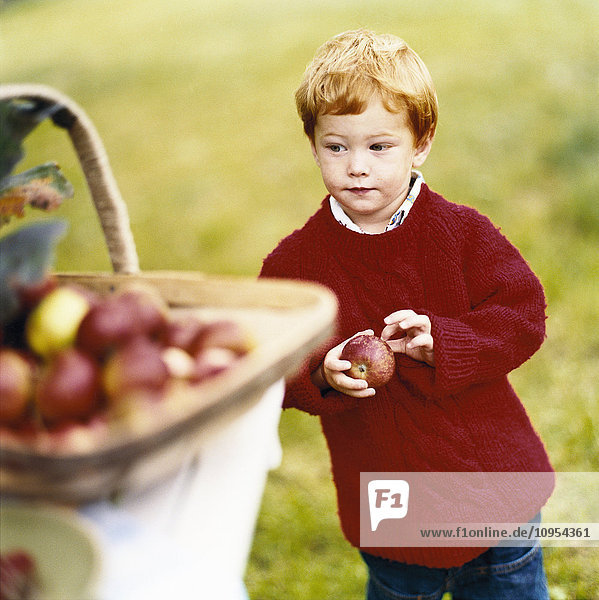 Junge im roten Hemd hält Apfel.