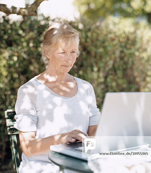 Ältere Frau benutzt Laptop im Garten