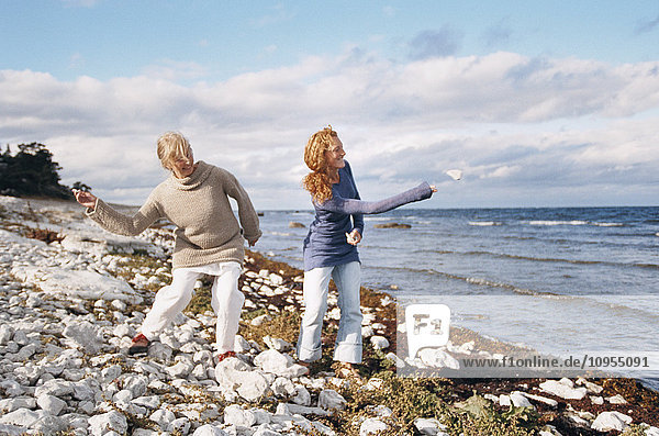 Mother and adult daughter throwing stones at sea