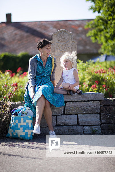 Mother and daughter sitting on a stone wall  Sweden.