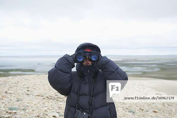 Teenager schaut durch ein Fernglas auf dem Mount Pelly  Ovayok Territorial Park  nahe Cambridge Bay; Nunavut  Kanada'.