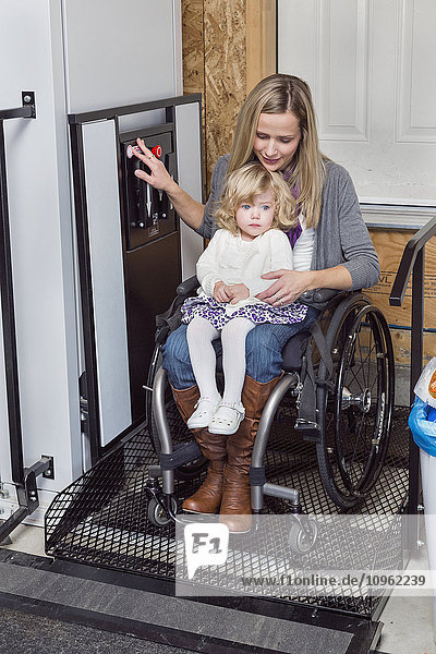 'Young disabled mother with her daughter using wheelchair powered device to assist with mobility; Spruce Grove Alberta Canada'