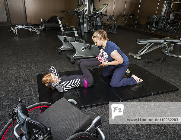 'Physiotherapist assisting young woman with spinal cord injury in performing double leg press exercises; Edmonton  Alberta  Canada'