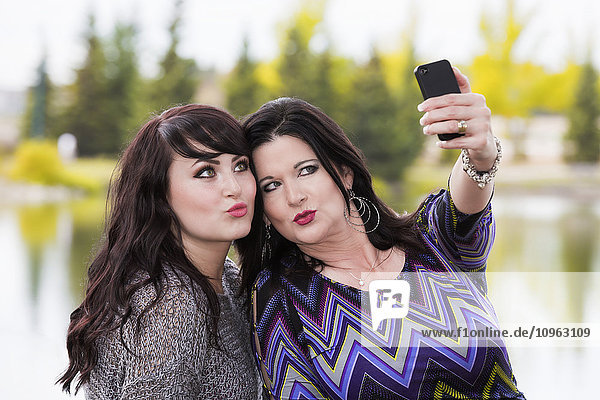 'Mother and daughter spending quality time together and taking a selfie outdoors in a city park in autumn; St. Albert  Alberta  Canada'