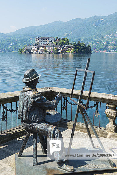 Statue eines Künstlers  der an einer Staffelei sitzt und malt  mit Blick auf die Insel San Giulio im Ortasee; Orta  Piemont  Italien'.