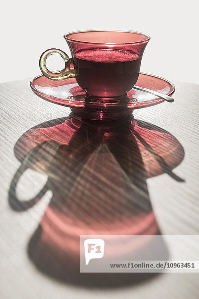 'A red glass cup a saucer with a beverage reflected on a white surface; Locarno  Ticino  Switzerland'