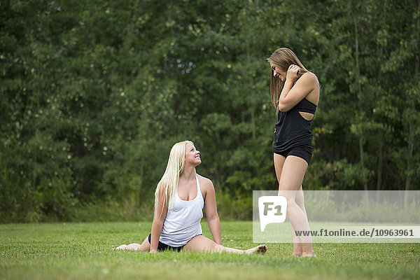 Zwei jugendliche Turnerinnen halten inne  um sich zu unterhalten  während sie Dehnübungen für ihre Turnübung machen; Edmonton  Alberta  Kanada'.