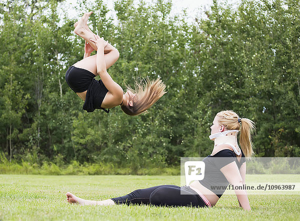 Eine jugendliche Turnerin übt im Freien in einem Park ihren Rückenschwung  während ihr verletzter Partner zusieht; Edmonton  Alberta  Kanada